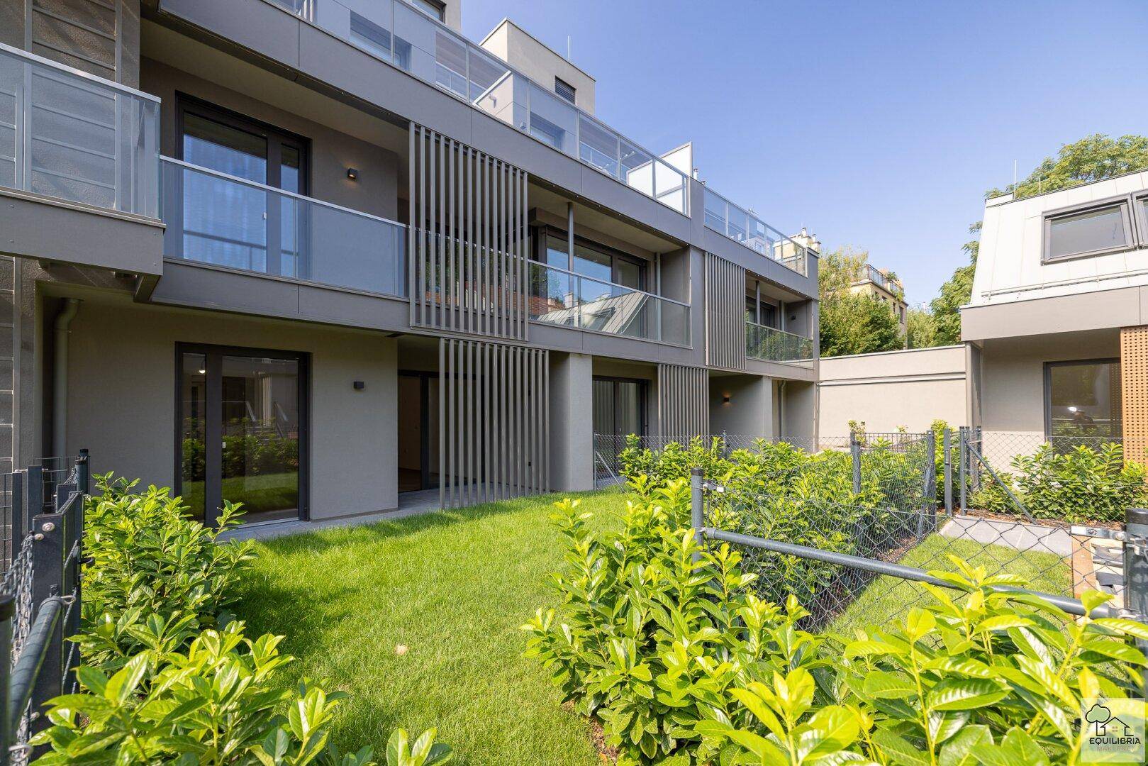 Moderne Wohnanlage mit Balkonen und einem gepflegten Gartenbereich im Erdgeschoss.