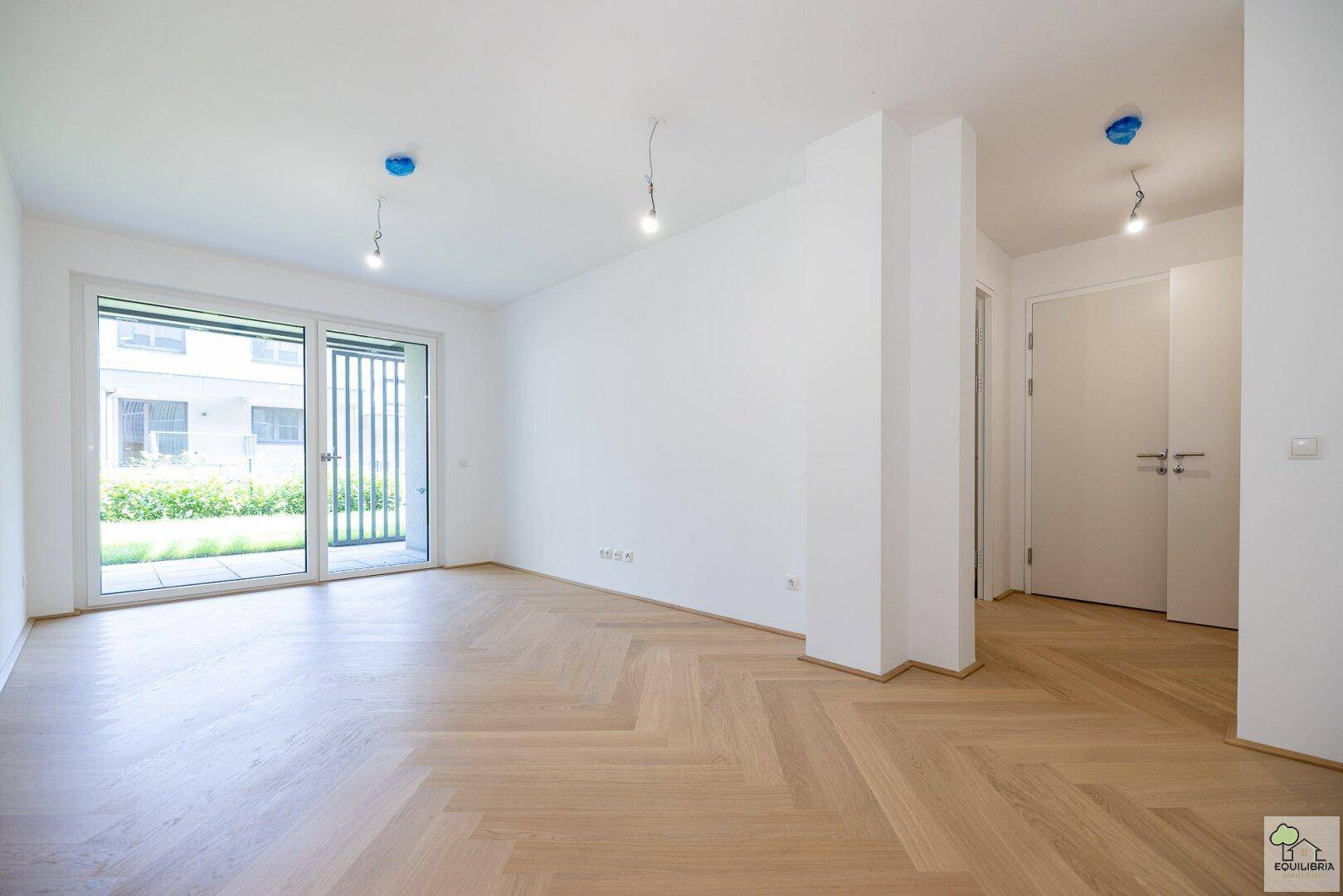 Heller, leerer Raum mit modernem Fischgrätparkett und großer Terrassentür zum Außenbereich.