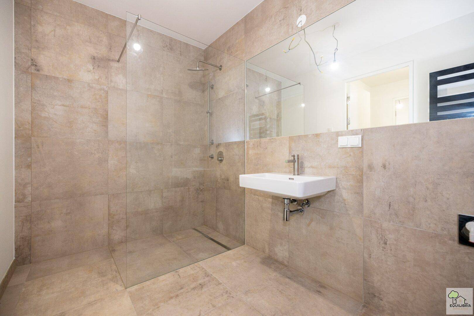 Modernes Badezimmer mit großer begehbarer Dusche und einem einzelnen Waschbecken, komplett gefliest.