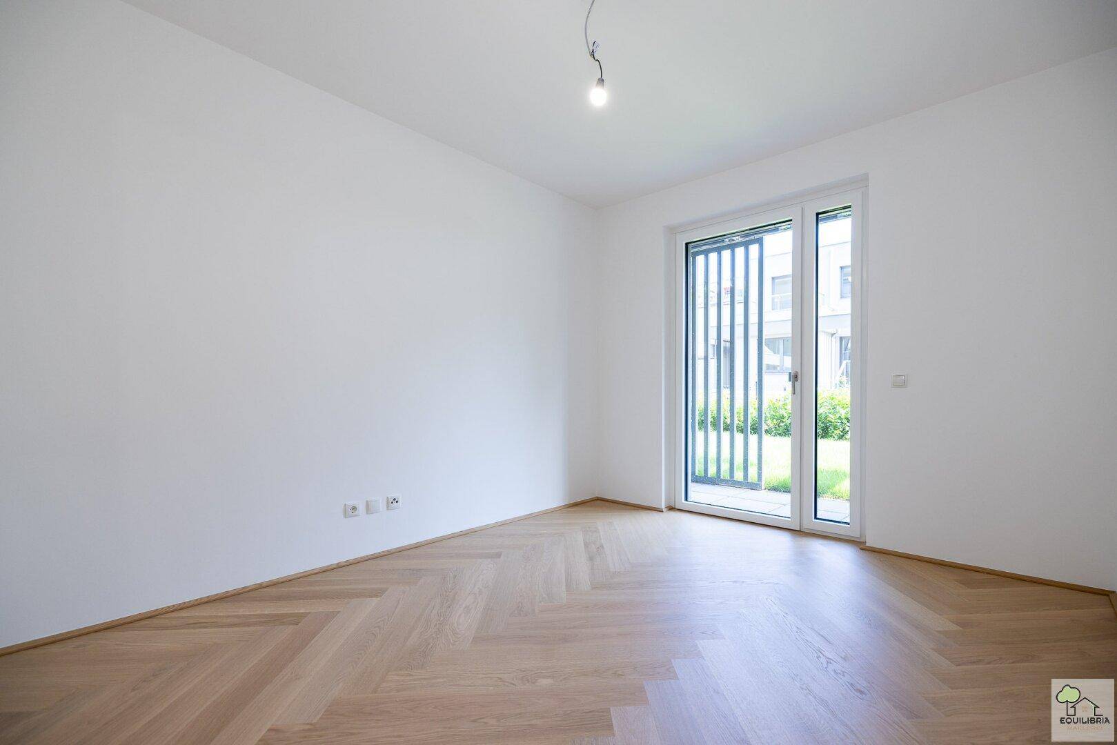 Helles, leeres Zimmer mit elegantem Fischgrätparkett und Zugang zu einem Außenbereich.