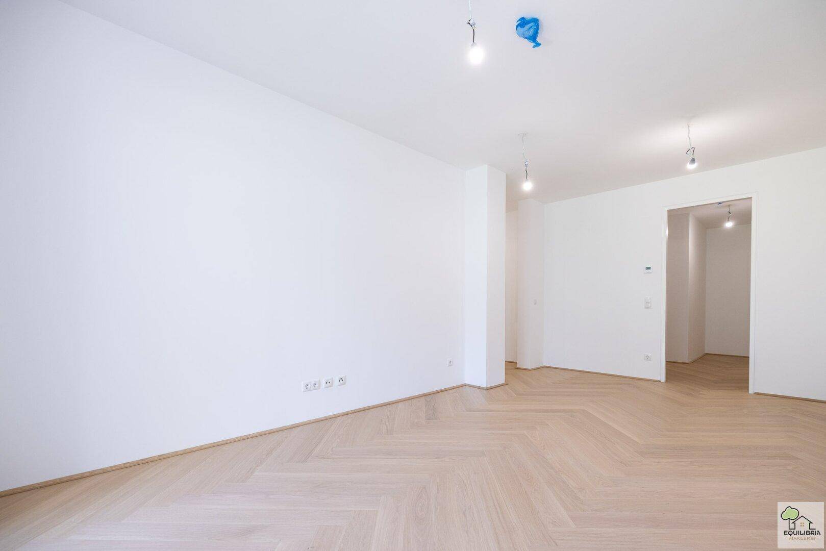 Großer, heller Raum mit elegantem Fischgrätparkett und mehreren Türöffnungen.