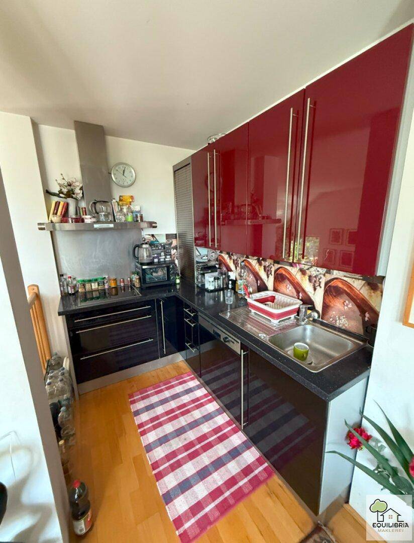 Moderne Küche mit roten Hochglanzschränken, dunkler Arbeitsplatte und Holzboden.