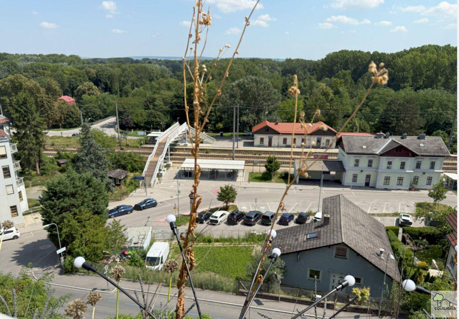 Weitläufiger Blick auf die Umgebung mit Bahnhof, Bäumen und Wohngebäuden.