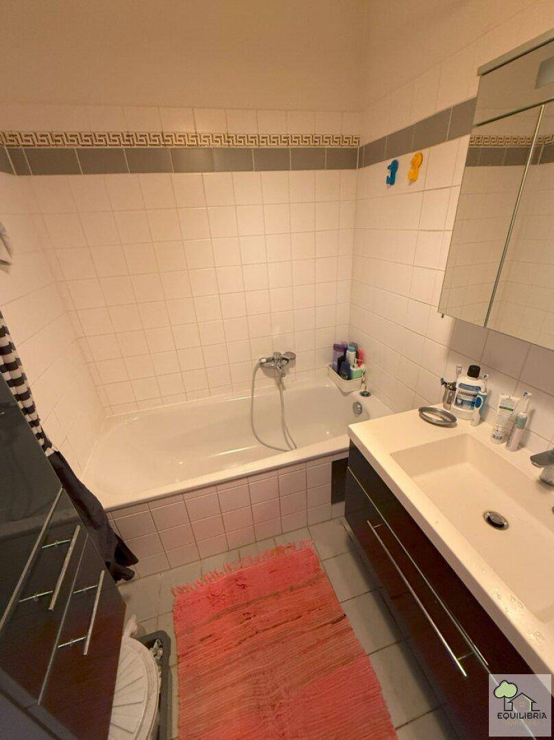 Badezimmer mit Badewanne, Waschbecken und Wandspiegel, gefliest in Weiß und Grau.