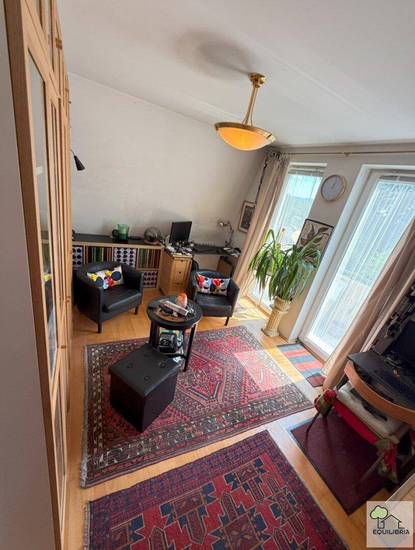 Heller Wohnbereich mit Sitzgelegenheiten, Schreibtisch und Zugang zu einem Balkon.
