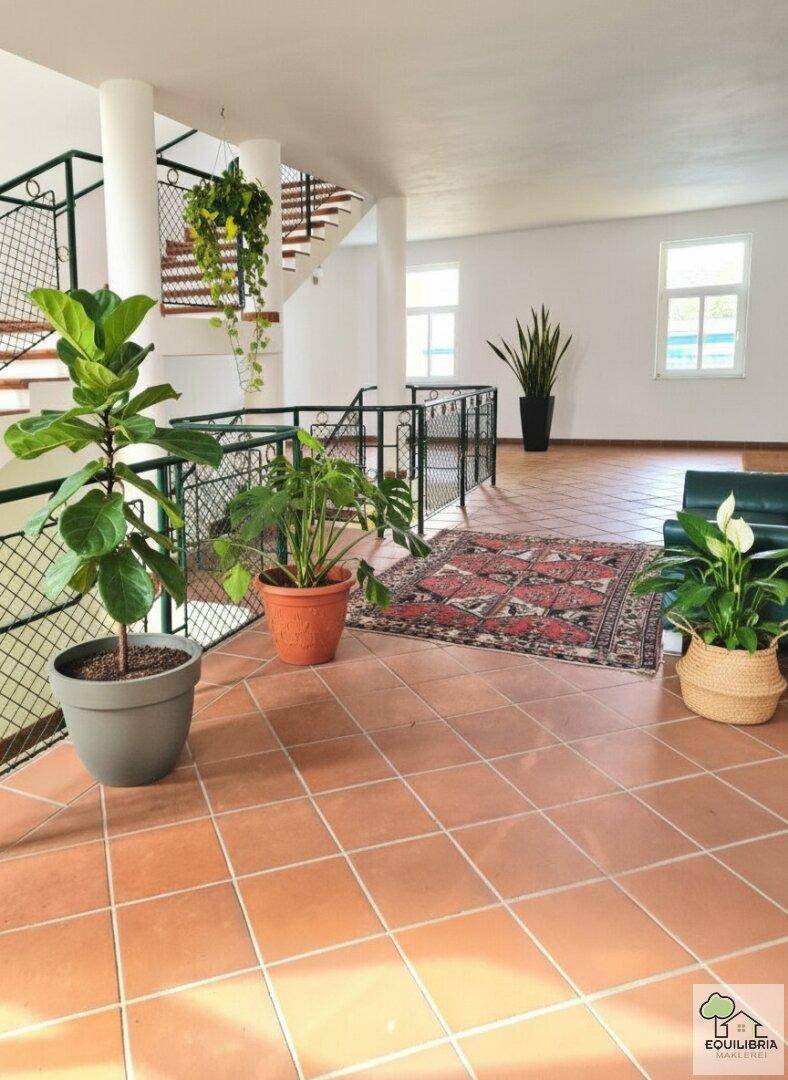Geräumiger Eingangsbereich mit Terrakottafliesen, Säulen und einer geschwungenen Treppe mit Metallgeländer.
