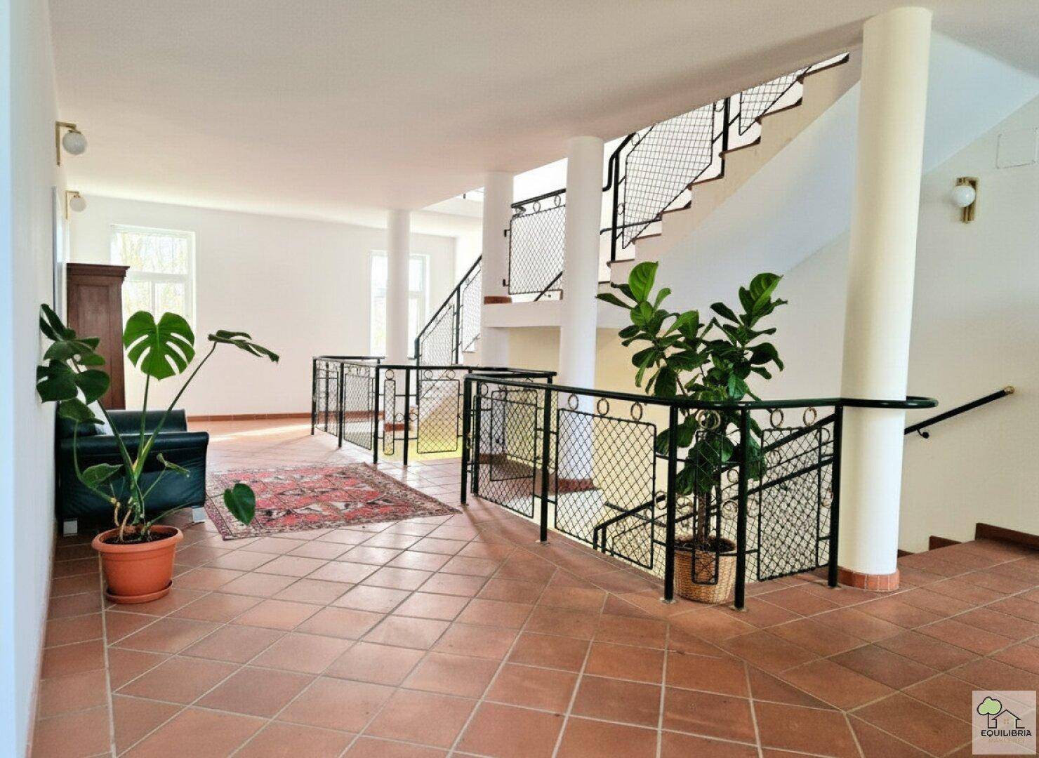 Heller Flur mit Terrakottafliesen, Säulen und einer eleganten Treppe mit schmiedeeisernem Geländer.