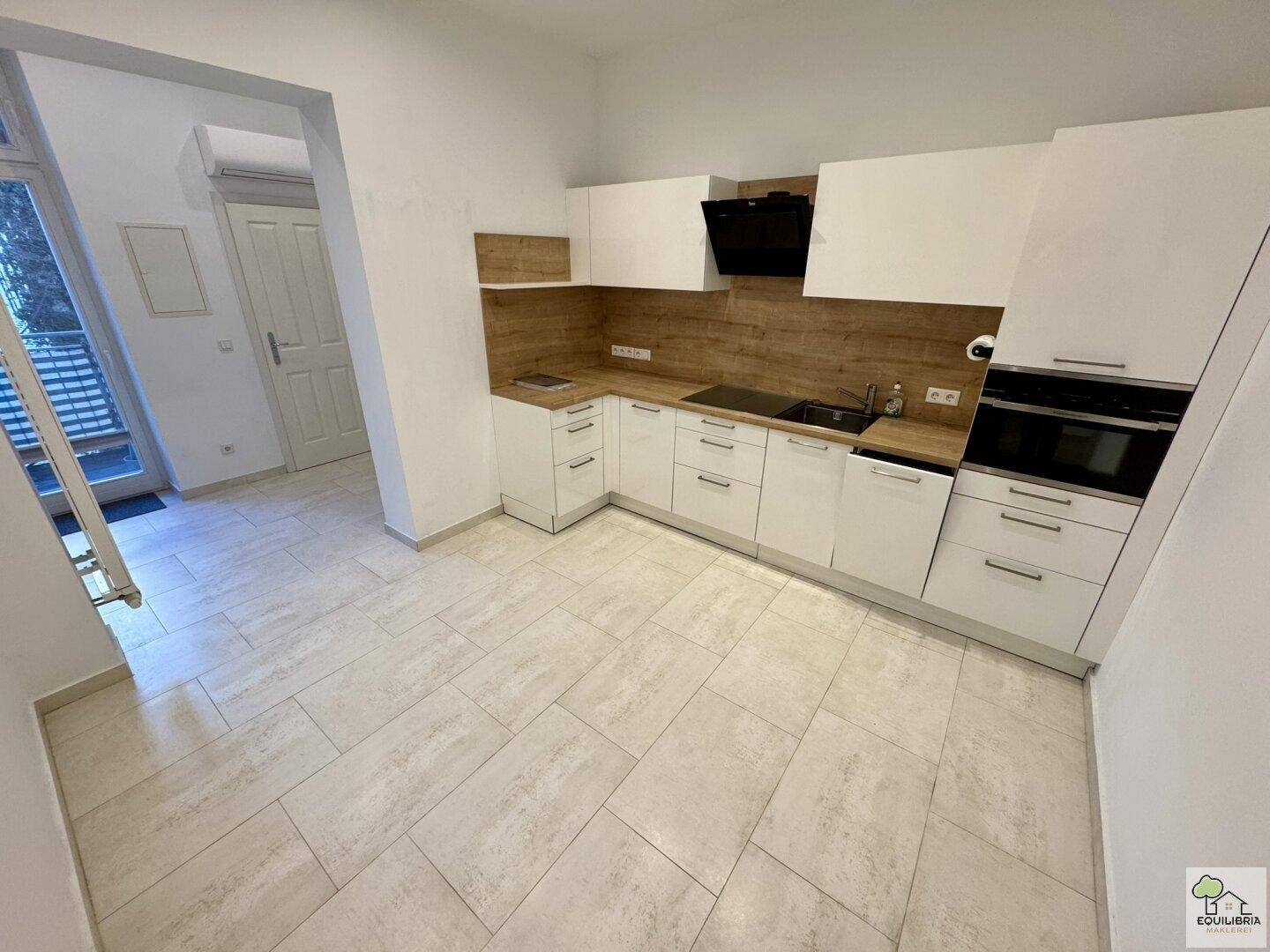 Moderne Küche mit weißen Schränken, Holzarbeitsplatten, Klimaanlage und Zugang zum Balkon.