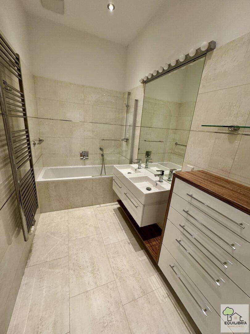 Modernes Badezimmer mit Doppelwaschbecken, Badewanne und einem praktischen beheizten Handtuchhalter.