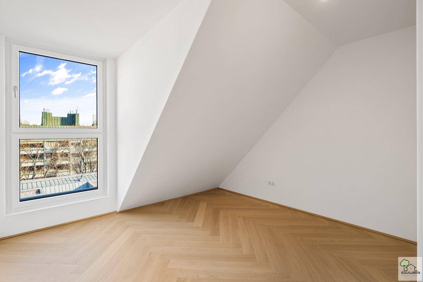 Helles Zimmer mit Dachschräge, großem Fenster und elegantem Fischgrätparkettboden.