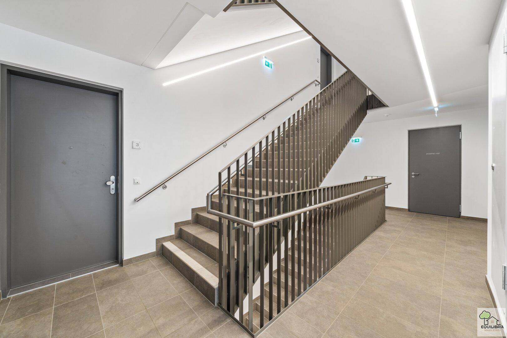 Modernes Treppenhaus mit Metallgeländer und Fliesenboden in einem Mehrfamilienhaus.
