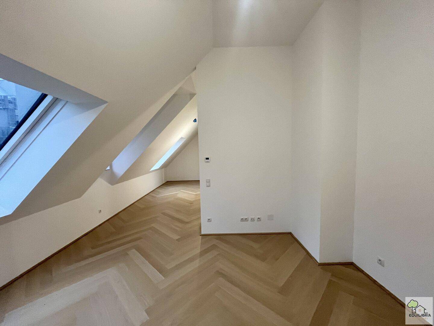 Helles Zimmer im Dachgeschoss mit Fischgrätparkett und mehreren Dachfenstern, ideal als Wohnbereich.