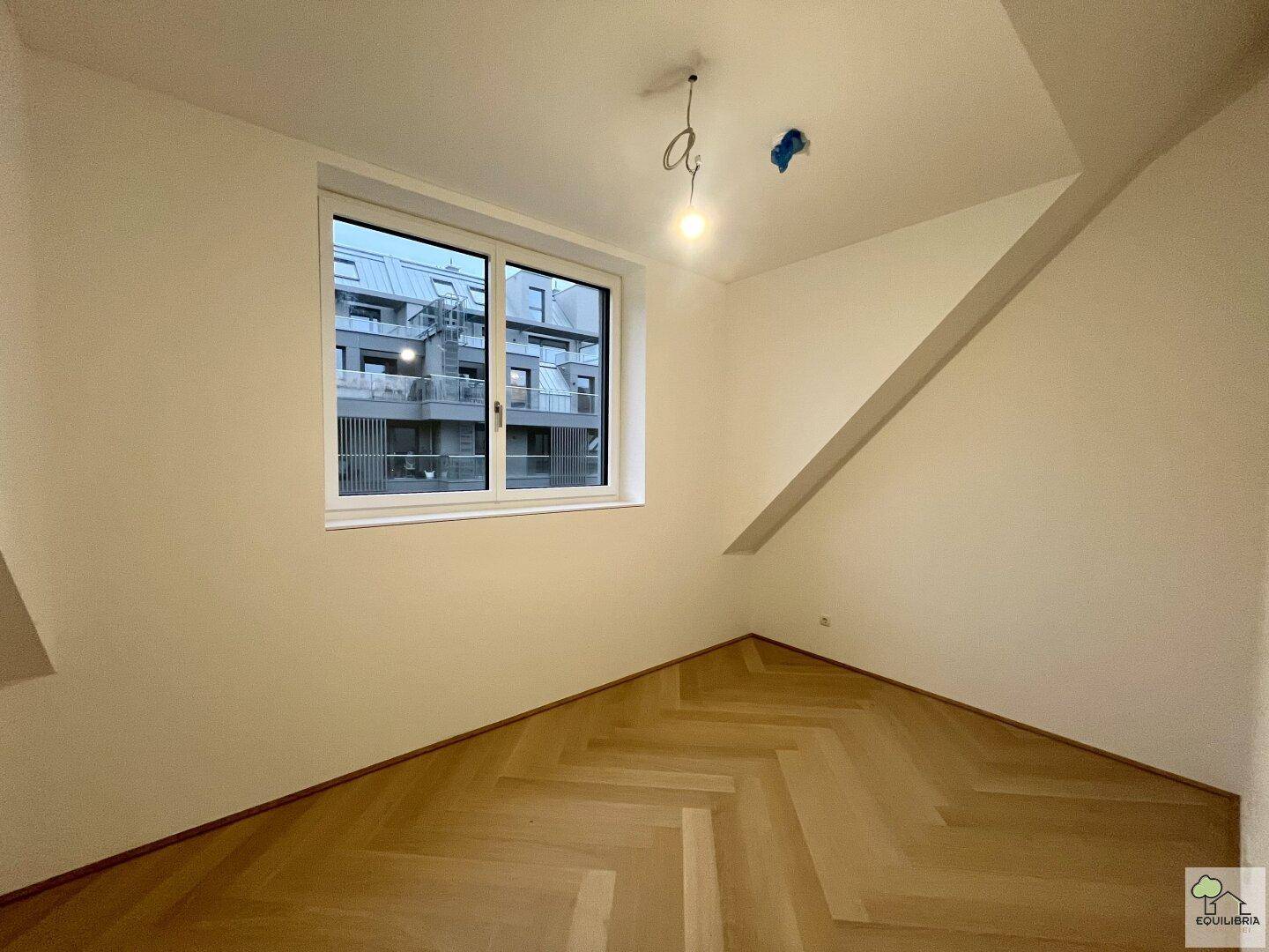 Helles Schlafzimmer im Dachgeschoss mit Fenster und neuem Fischgrätparkettboden, blickt auf den Innenhof.