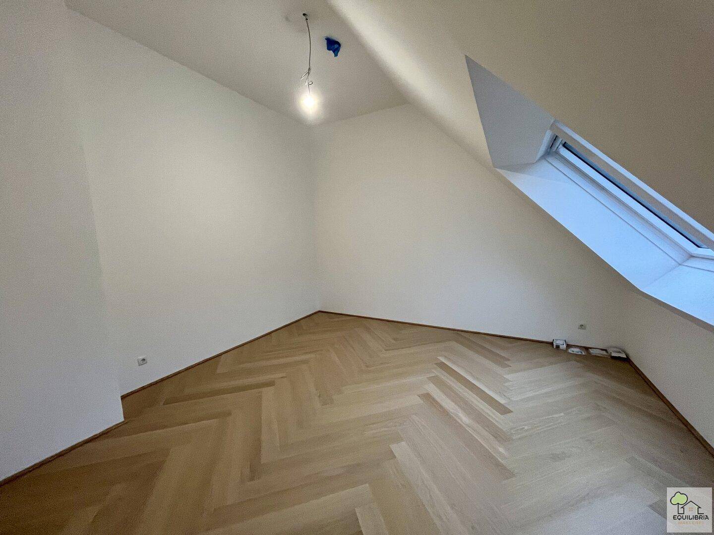 Geräumiges Zimmer im Dachgeschoss mit Dachfenster und elegantem Fischgrätparkettboden.