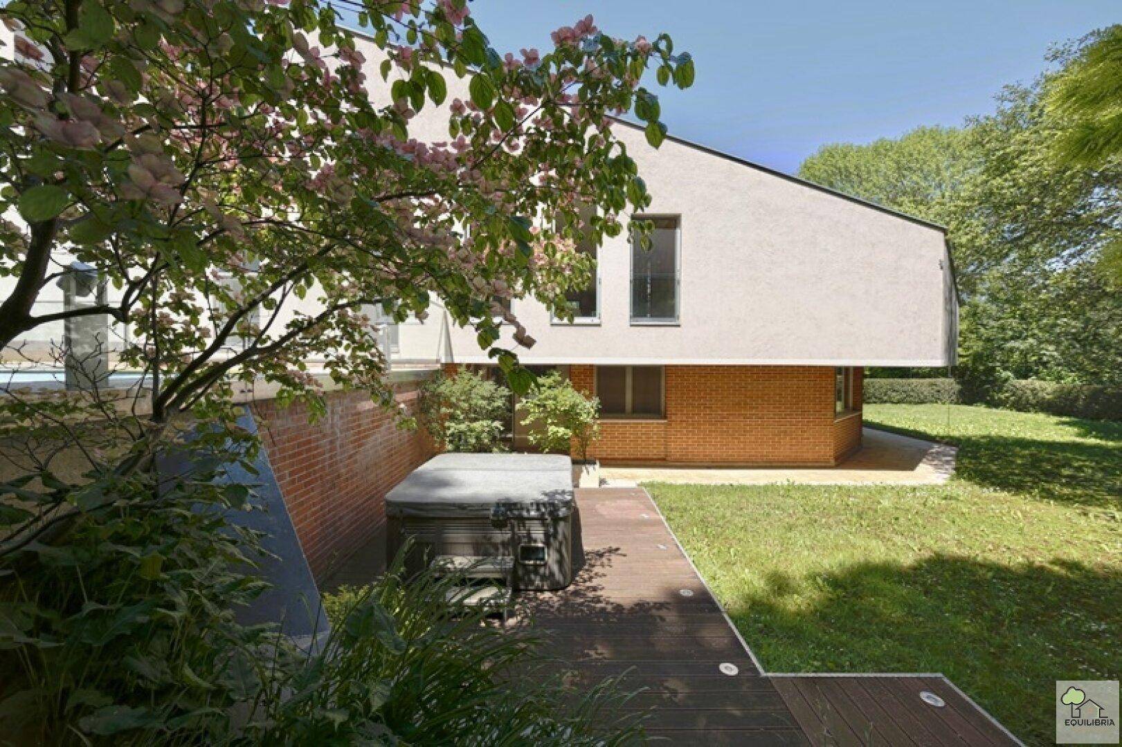 Außenbereich mit Whirlpool auf Holzdeck, umgeben von Grün und blühenden Bäumen.