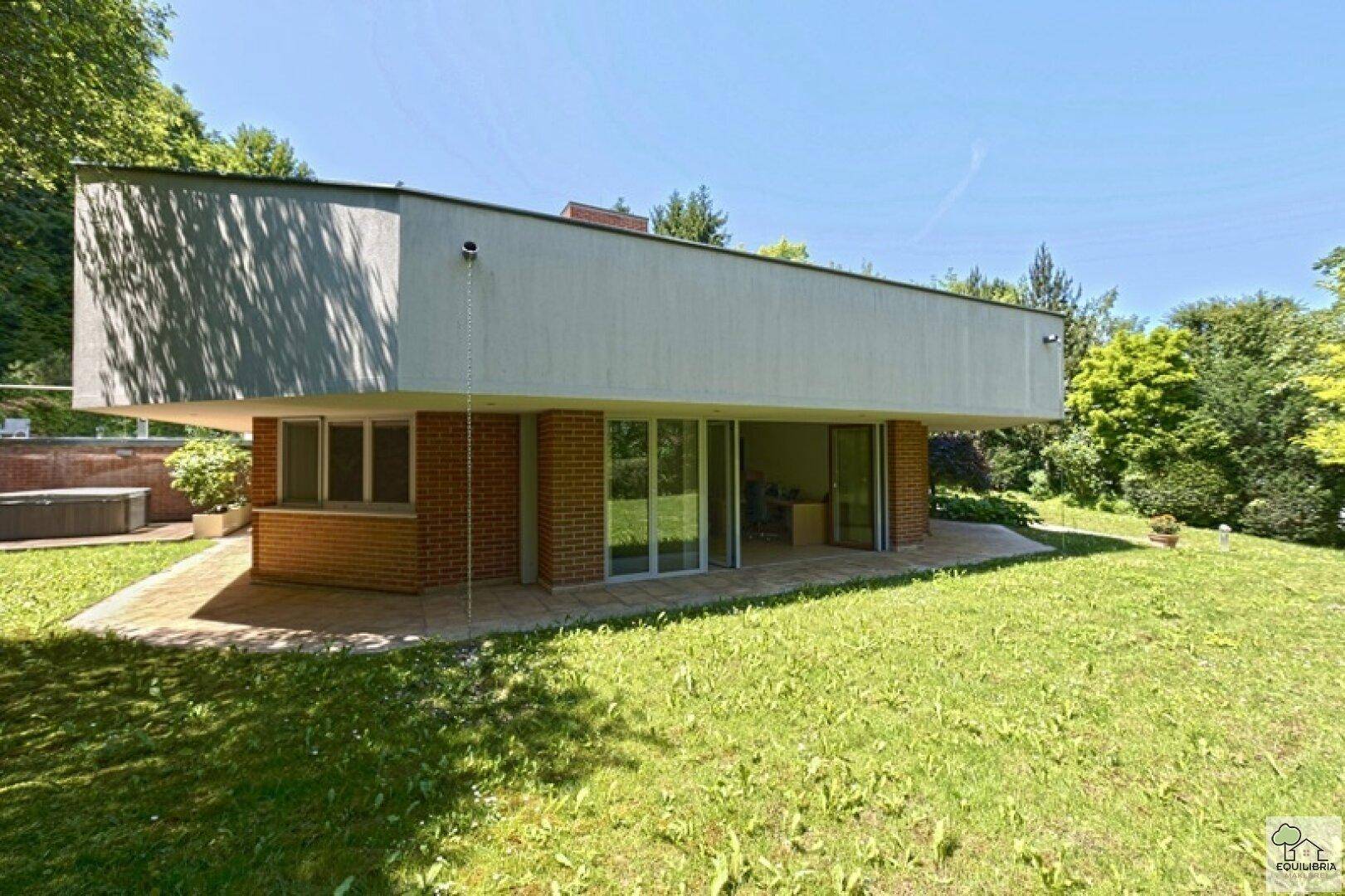 Rückseite des Hauses mit weitläufigem Rasen und großen Glasfronten zum Garten.