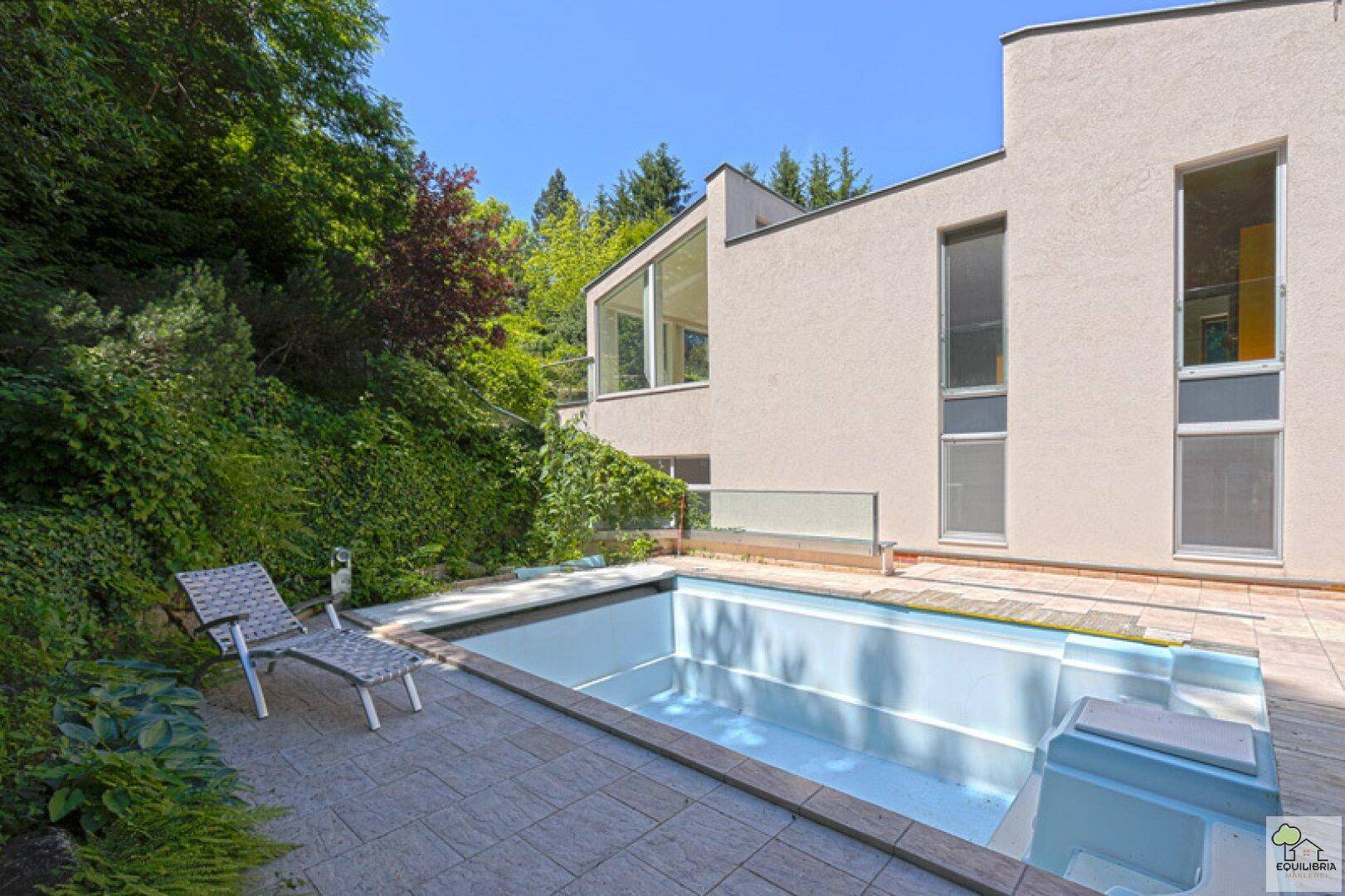 Außenansicht des Hauses mit Schwimmbecken und Liegestuhl, umgeben von viel Grün.