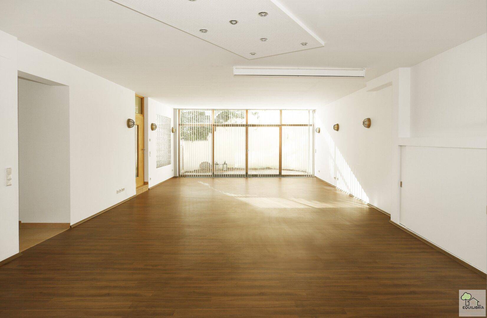 Großes, helles Wohnzimmer mit Holzboden und breiter Fensterfront, lichtdurchflutet.