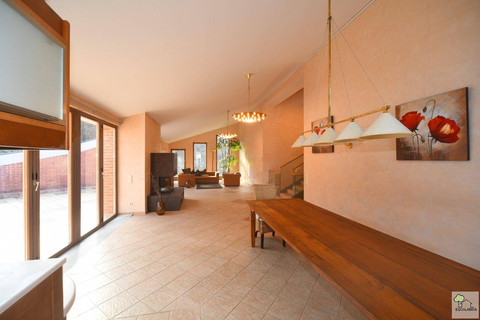 Offener Wohnbereich mit langem Esstisch, Kamin und Zugang zur Terrasse, sehr geräumig.