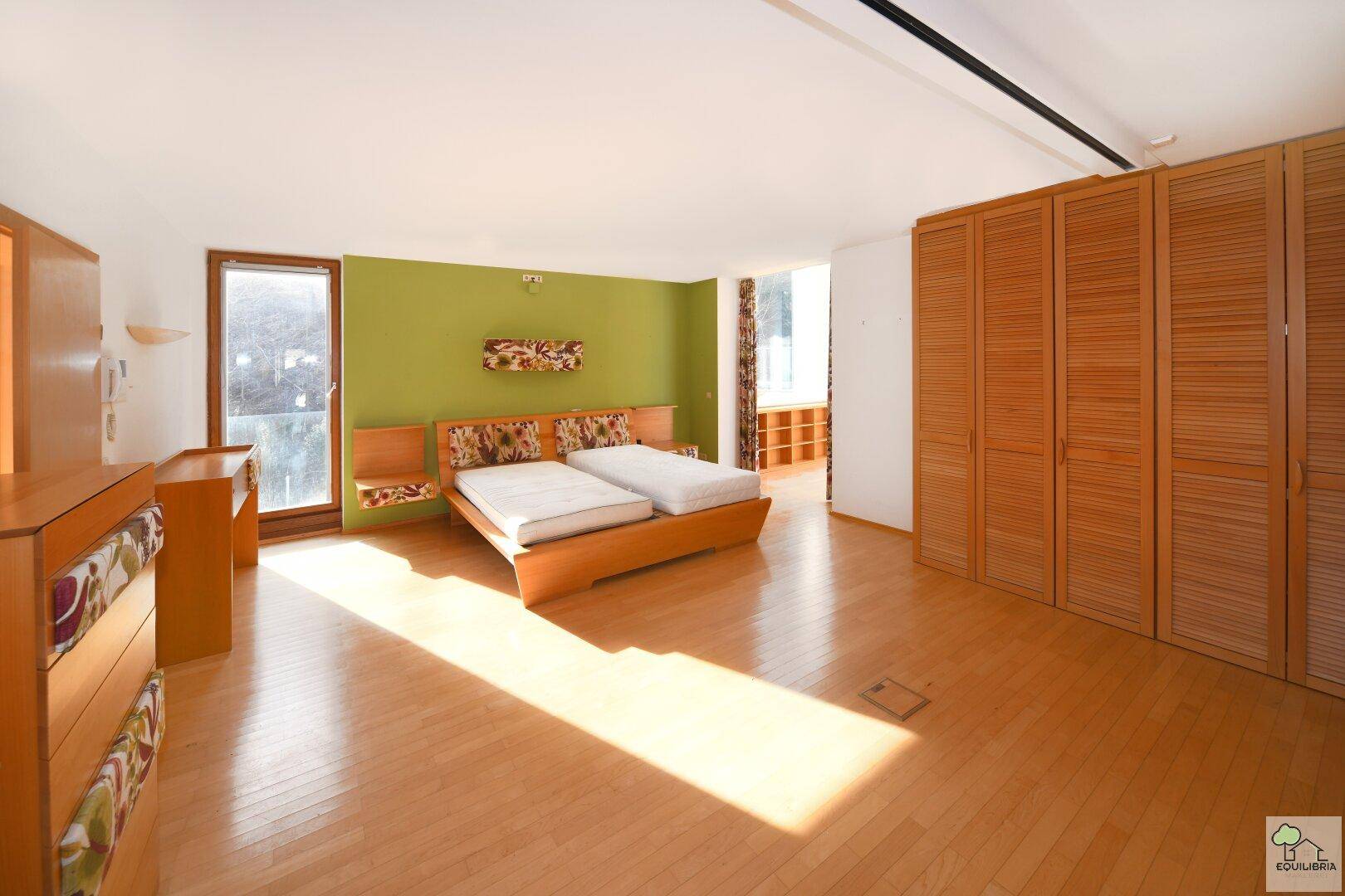 Geräumiges Schlafzimmer mit Holzboden, Einbauschränken und Zugang zum Balkon.