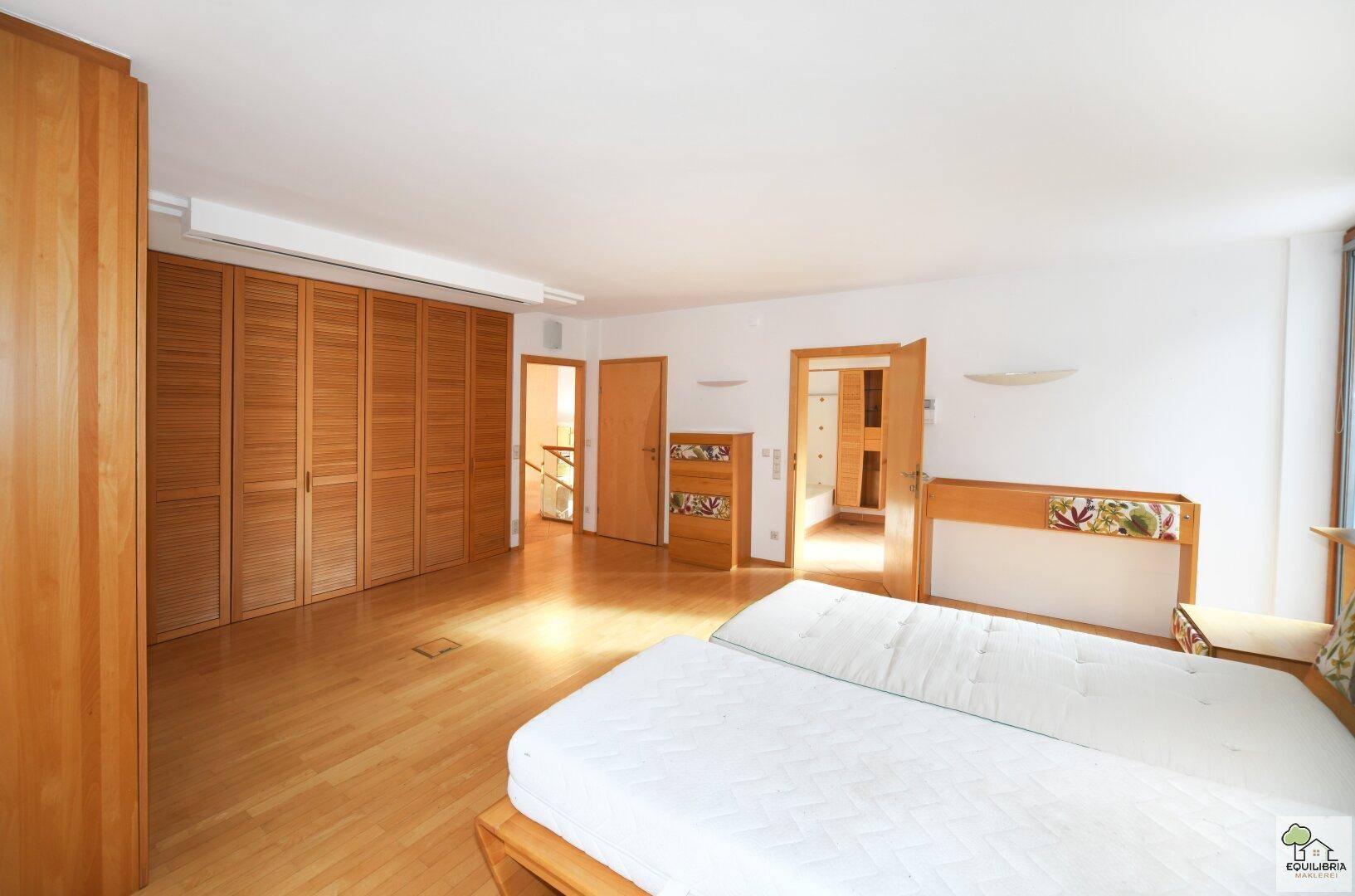 Schlafzimmer mit Holzboden, Einbauschränken und Zugang zu weiteren Räumen.