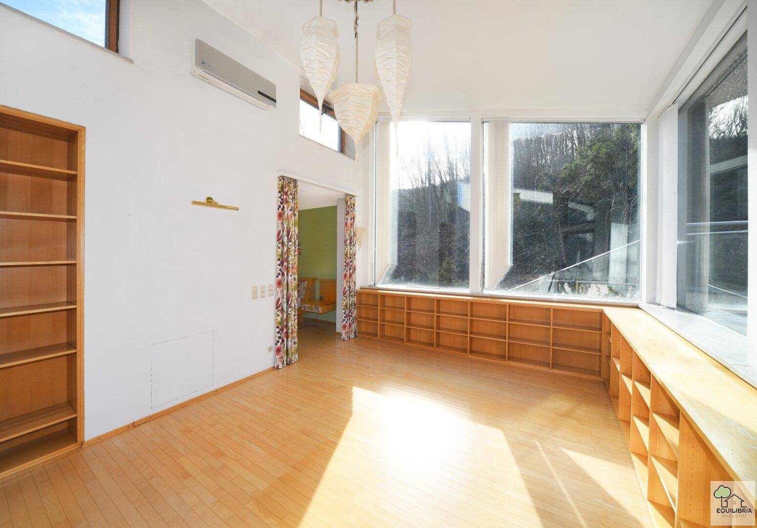 Lichtdurchfluteter Raum mit hohen Decken, Holzboden und Klimaanlage, ideal für Wohnzwecke.
