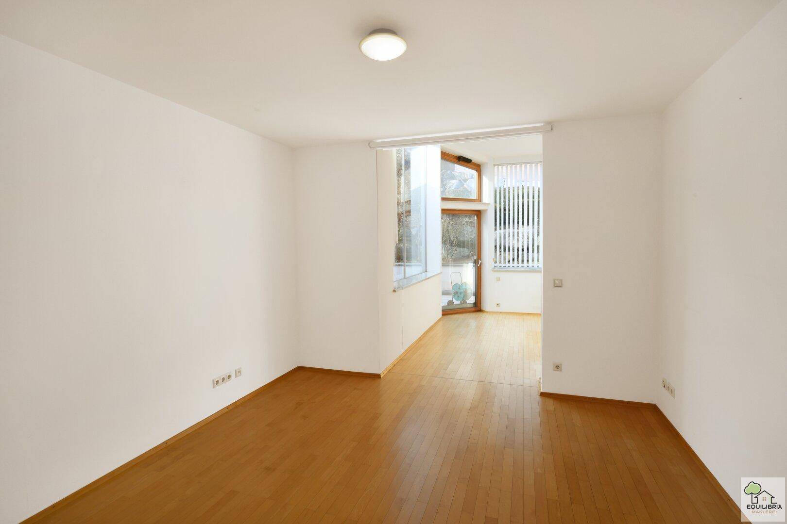 Heller, leerer Raum mit Holzboden und großen Fenstern, vielseitig nutzbar.