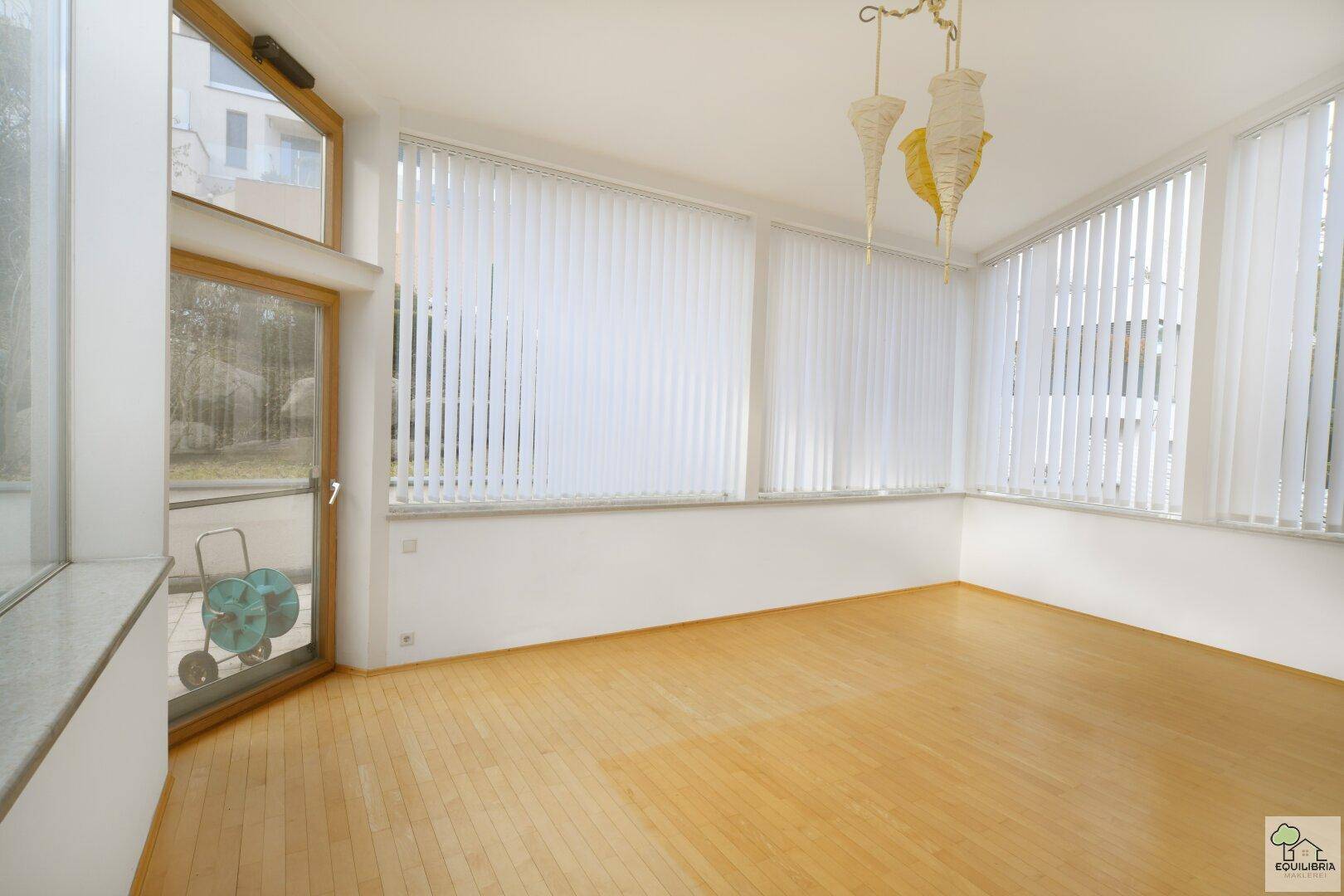Lichtdurchfluteter Wintergarten mit Holzboden und großen Fensterfronten, ideal zum Entspannen.
