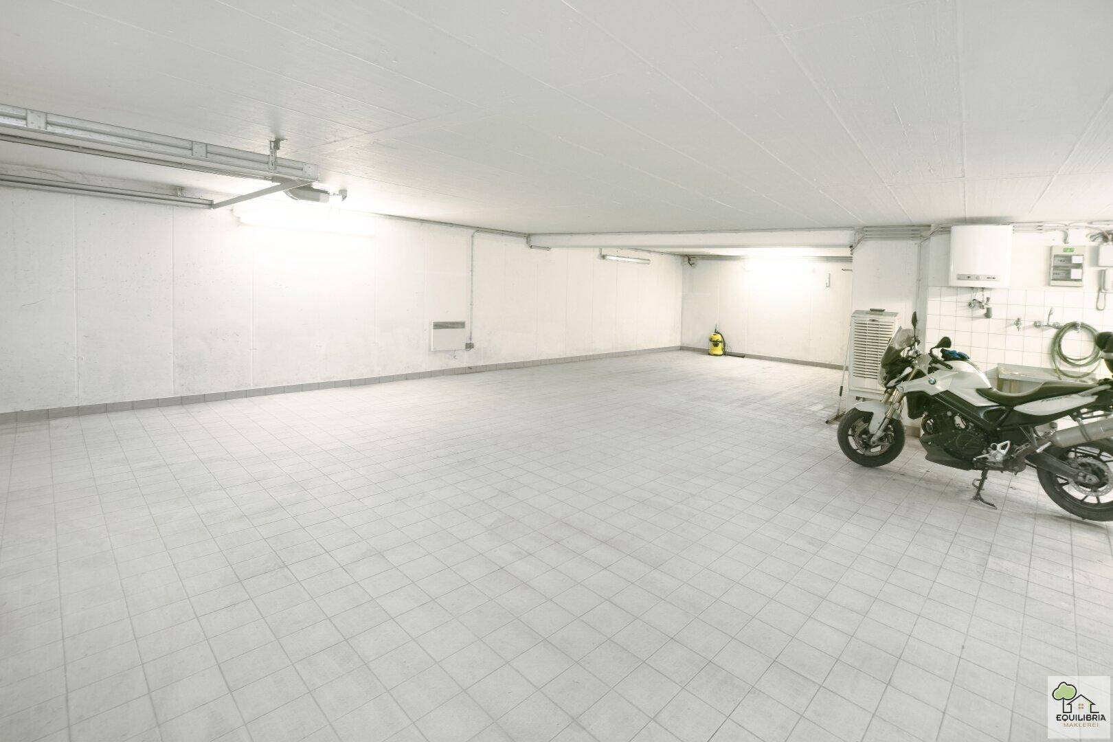 Geräumige Garage mit Fliesenboden und Platz für mehrere Fahrzeuge und Motorräder.