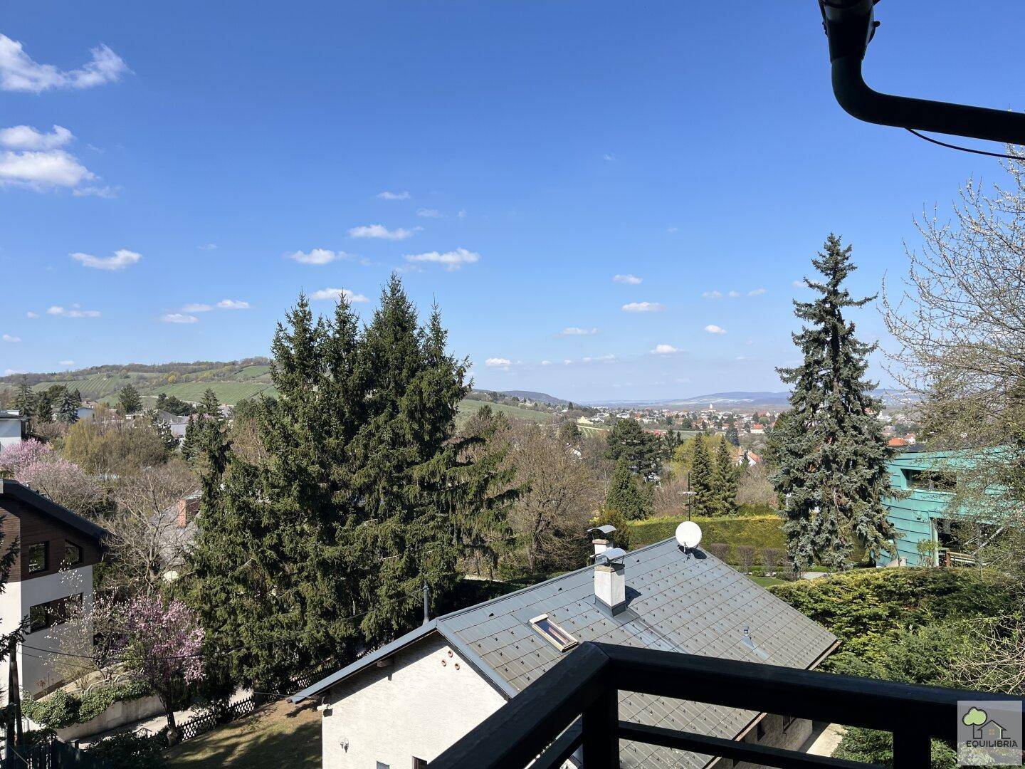 Panoramablick über eine bewaldete Hügellandschaft mit verstreuten Häusern unter blauem Himmel.