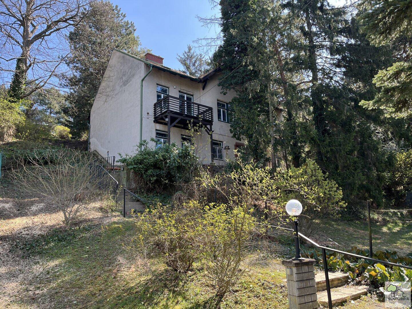 Wohnhaus auf einem Hanggrundstück mit Garten, umgeben von Bäumen und Sträuchern.