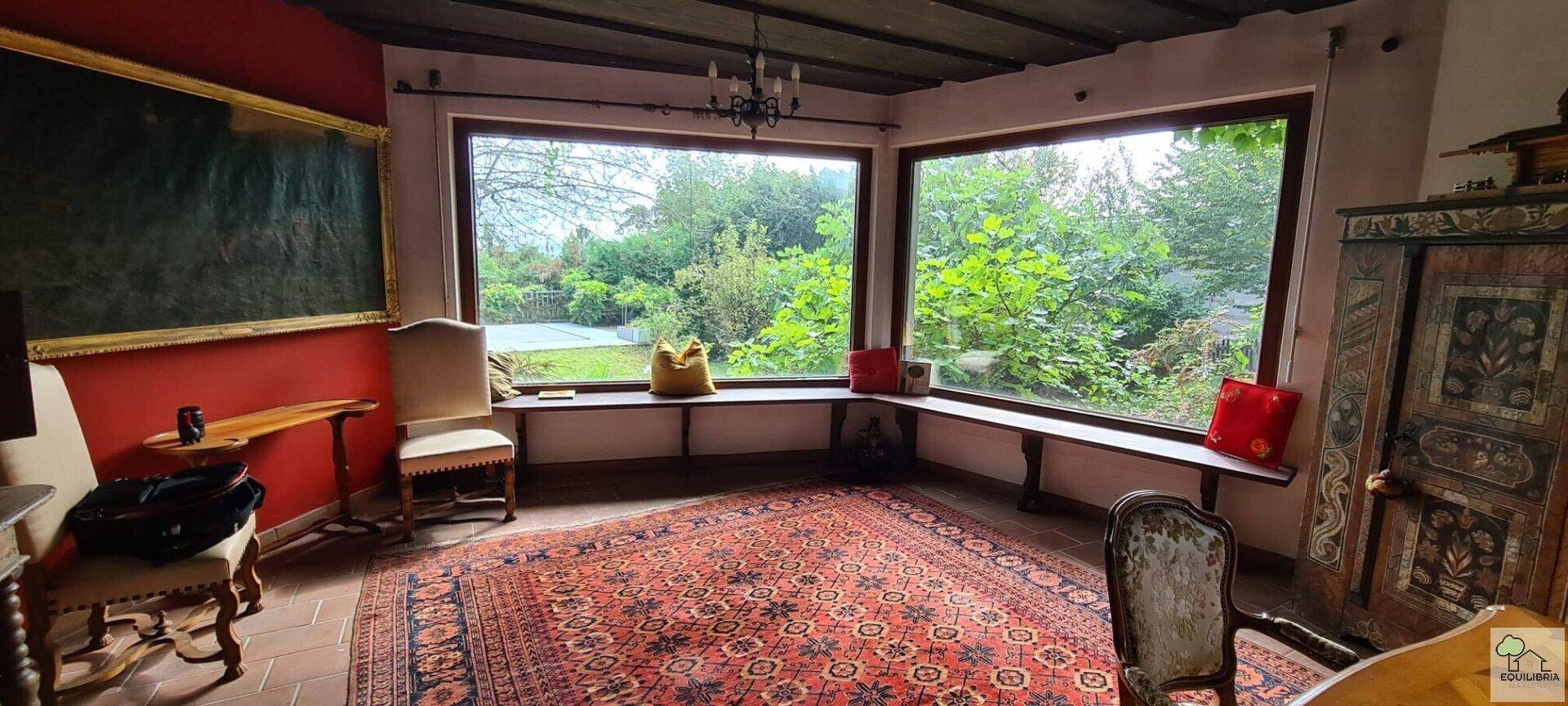 Gemütliches Wohnzimmer mit großen Eckfenstern, die einen weiten Blick ins Grüne bieten.