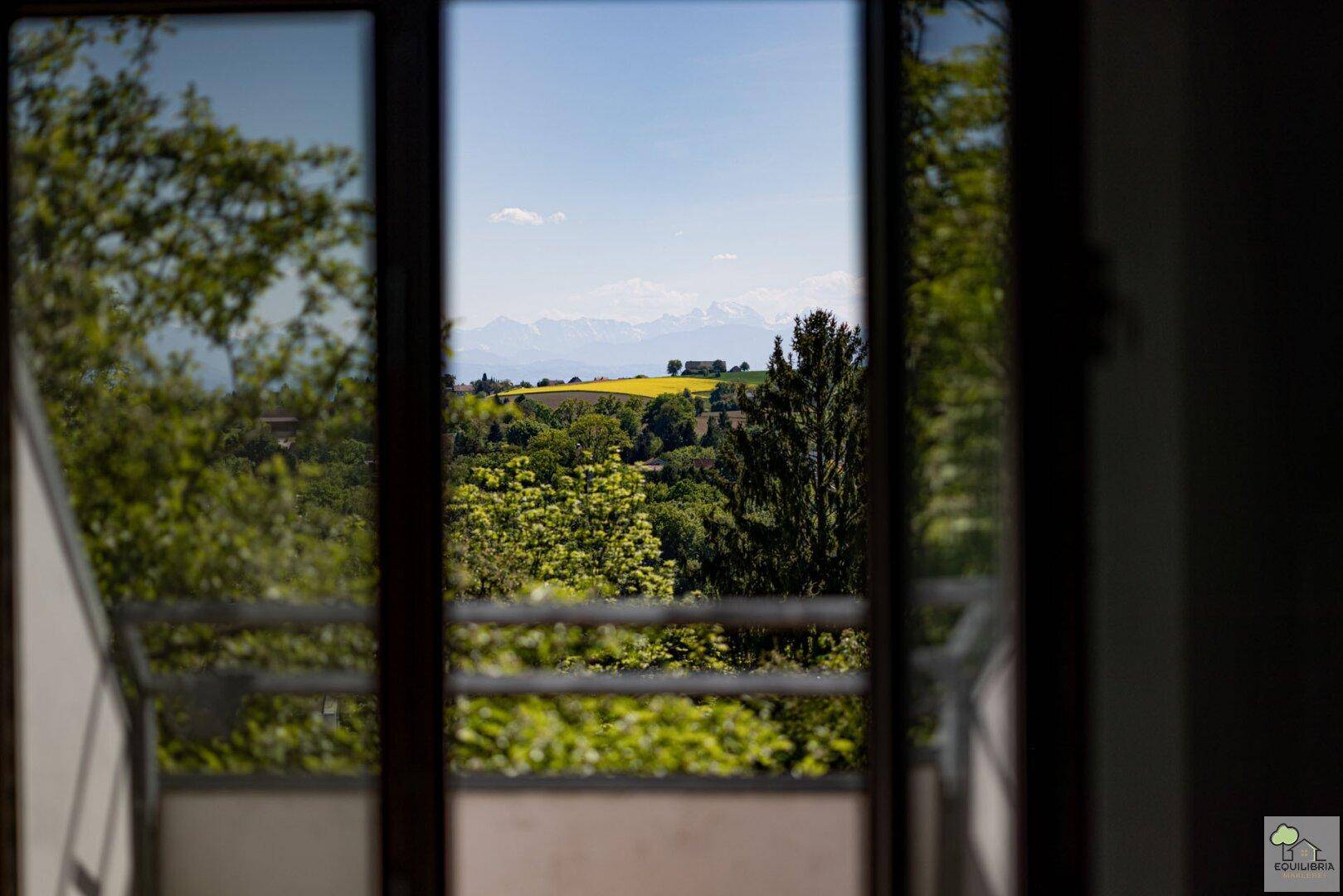 Panoramablick aus dem Fenster auf eine weite Landschaft mit grünen Hügeln und fernen Bergen.