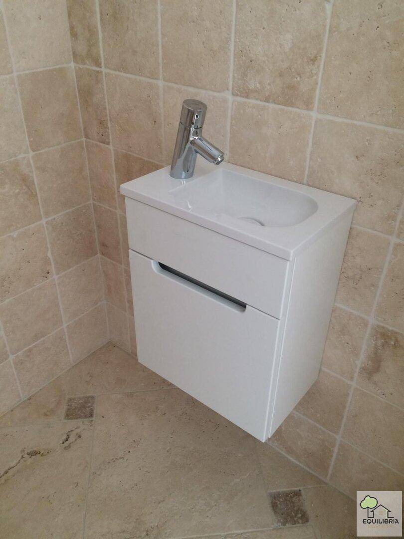 Modernes Einzelwaschbecken mit Unterschrank und beigefarbenen Fliesen an Wänden und Boden.