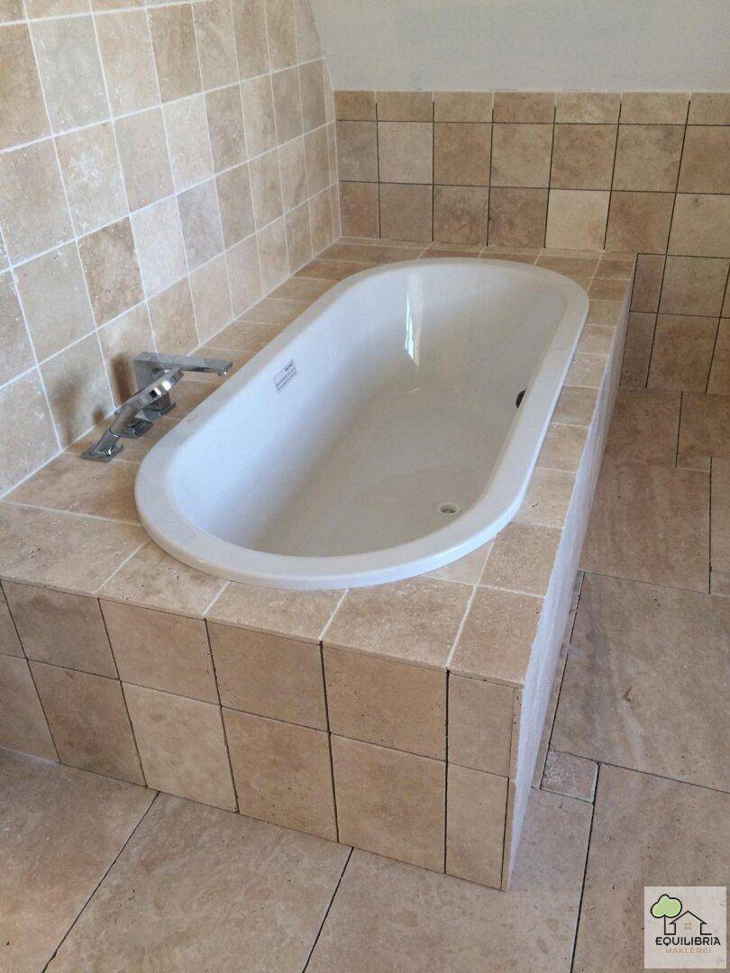 Eingebaute Badewanne mit beigefarbenen Fliesen und moderner Armatur.
