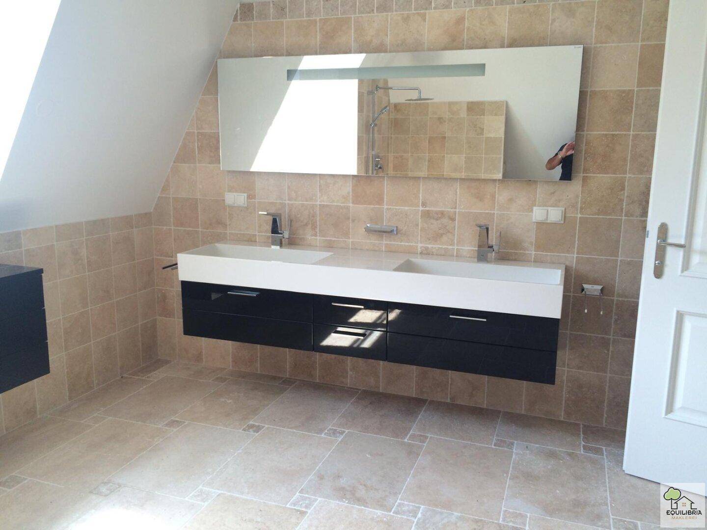 Helles Badezimmer mit Doppelwaschbecken, großem Wandspiegel und beigefarbenen Fliesen.