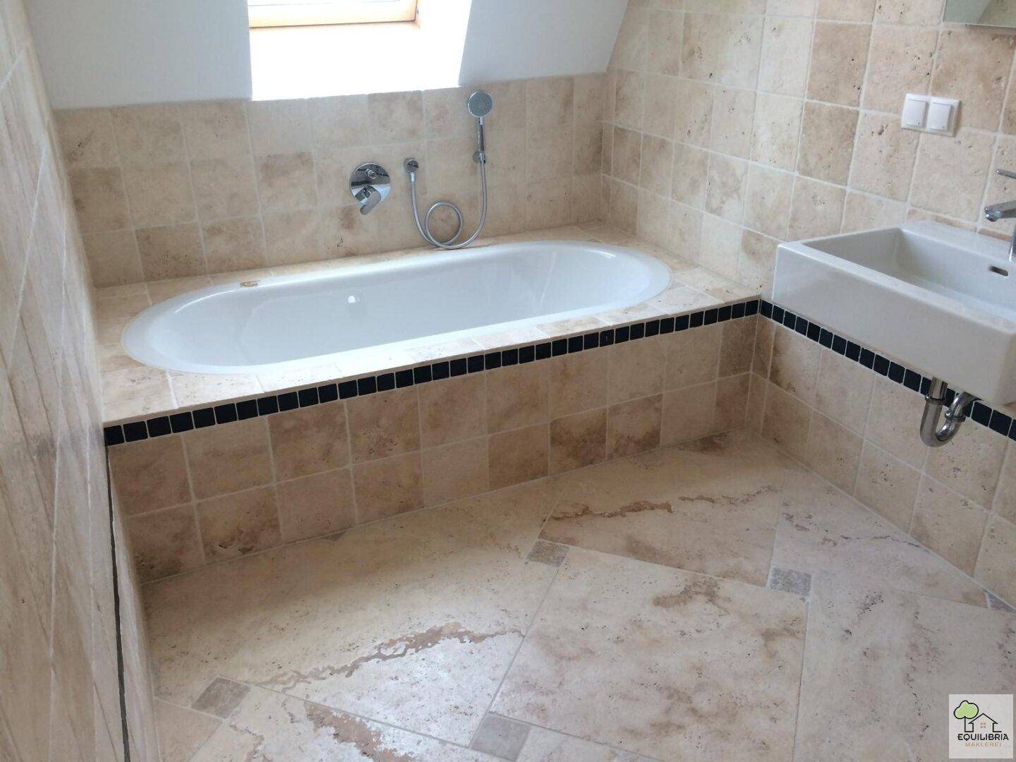 Badezimmer mit Badewanne, Einzelwaschbecken und beigefarbenen Fliesen im Dachgeschoss.