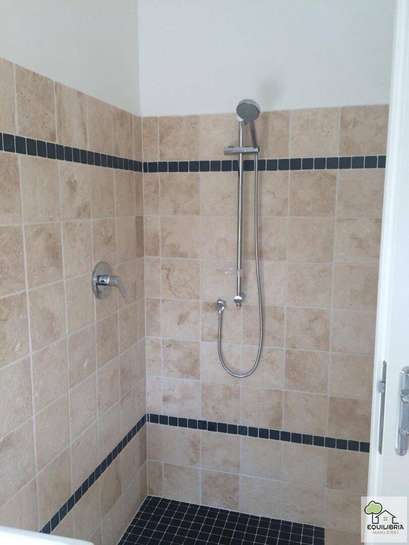 Duschbereich mit beigefarbenen Wandfliesen und dunklem Boden in modernem Design.