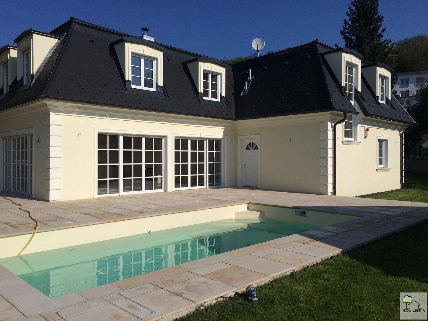 Elegantes Haus mit Swimmingpool und gepflegtem Gartenbereich unter blauem Himmel.