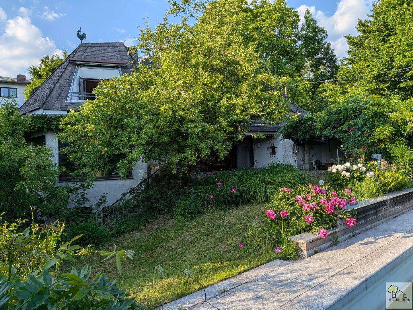 Charmantes Haus mit üppigem Garten und blühenden Blumenbeeten in sonniger Lage.