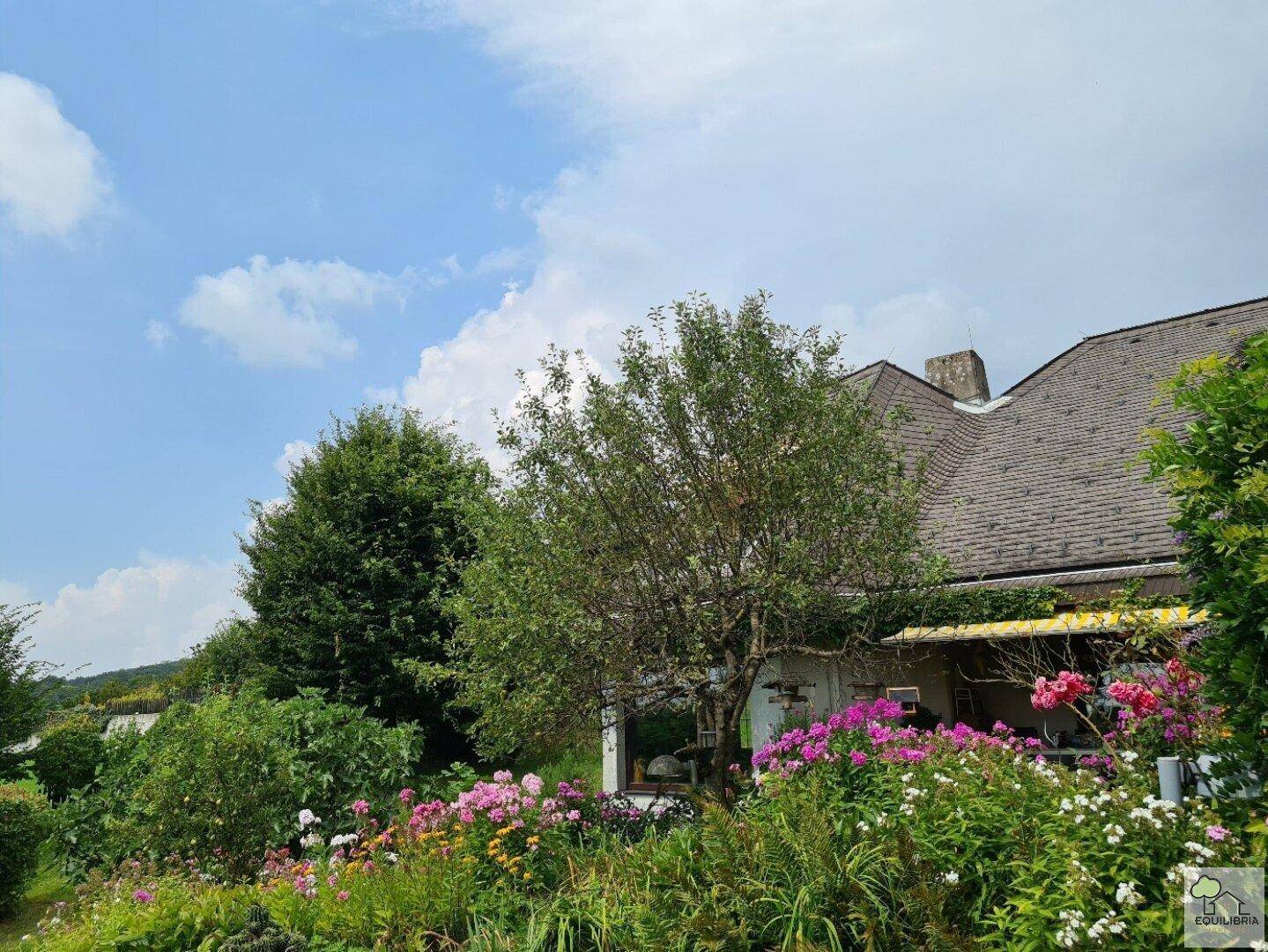 Malerischer Gartenbereich mit blühenden Blumen und Bäumen vor der Fassade des Hauses.