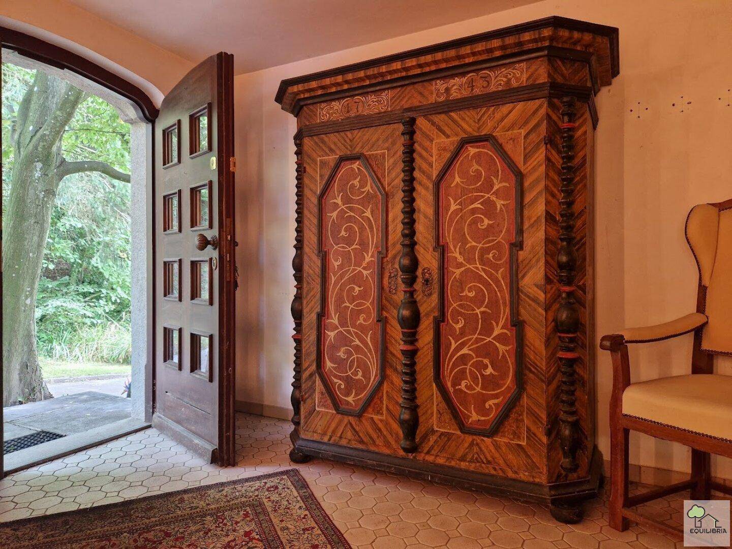 Eingangsbereich mit einem kunstvoll verzierten Holzschrank und offenem Zugang zum Außenbereich.