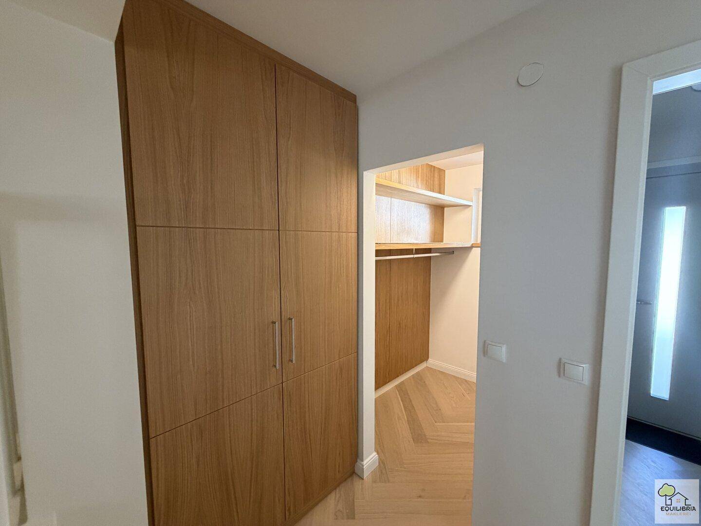 Heller Flur mit integrierten Holzschränken und Zugang zu einem begehbaren Kleiderschrank.