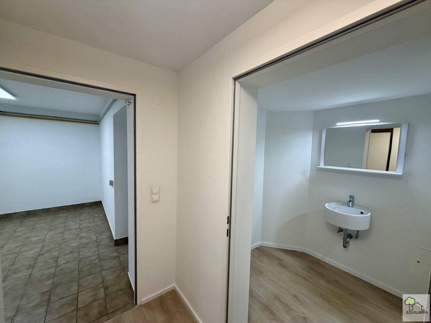 Kellerbereich mit kleinem Waschbecken und Zugang zu einem weiteren Raum.