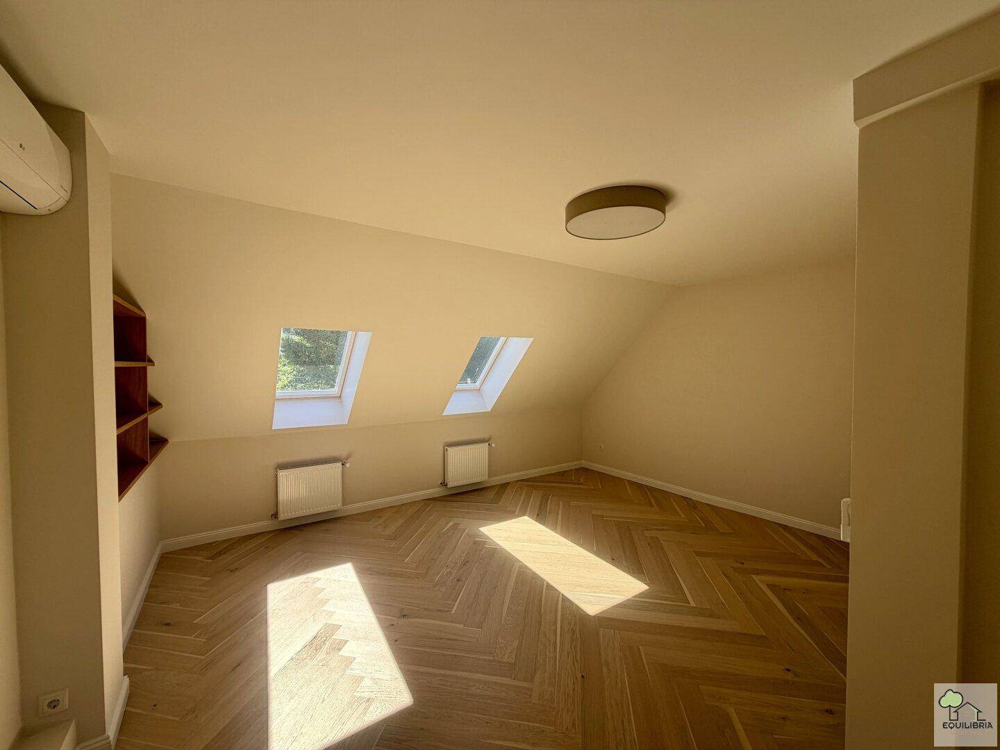 Helles Schlafzimmer im Dachgeschoss mit schrägen Wänden, Dachfenstern und Fischgrätparkett.