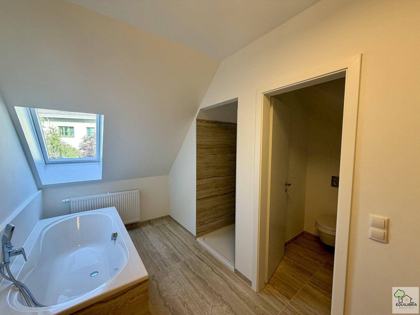Modernes Dachgeschossbad mit Badewanne, separater Dusche und Dachfenster für natürliches Licht.