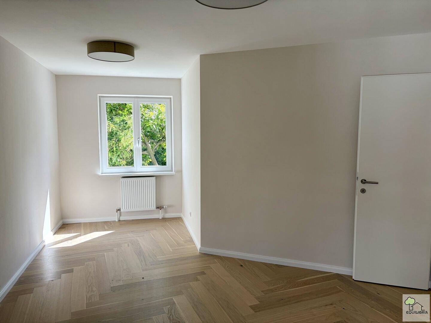 Geräumiges Schlafzimmer mit Fischgrätparkett und hellem Fenster, bietet viel Tageslicht.