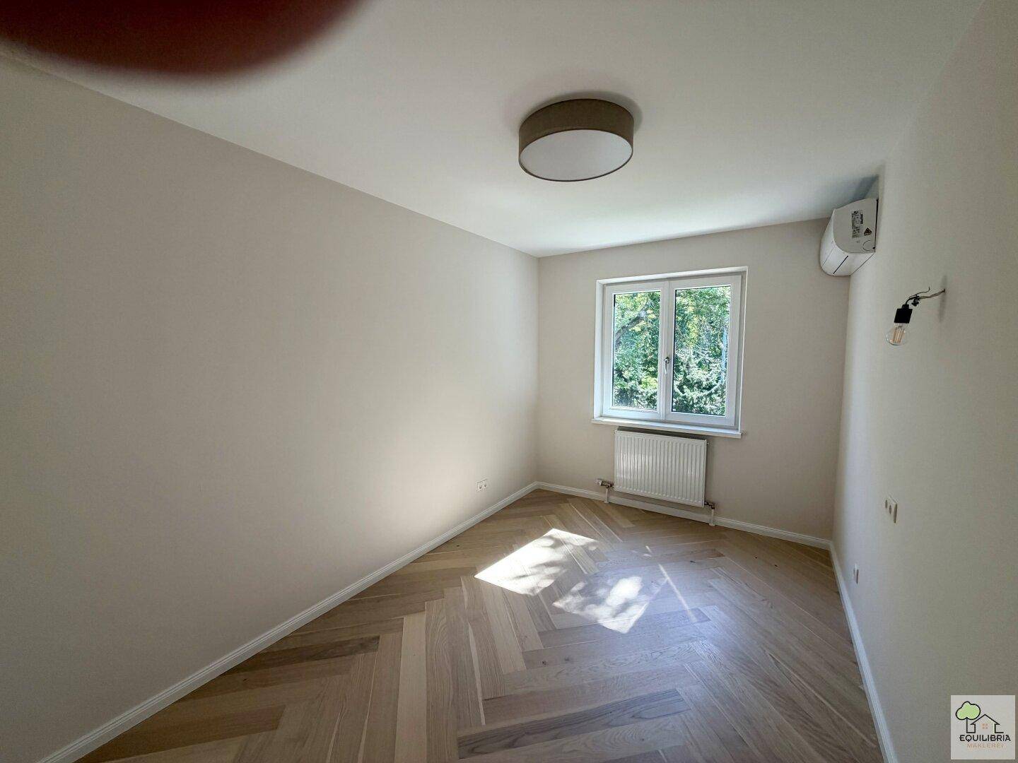 Helles Schlafzimmer mit Fischgrätparkett, Fenster und installierter Klimaanlage.