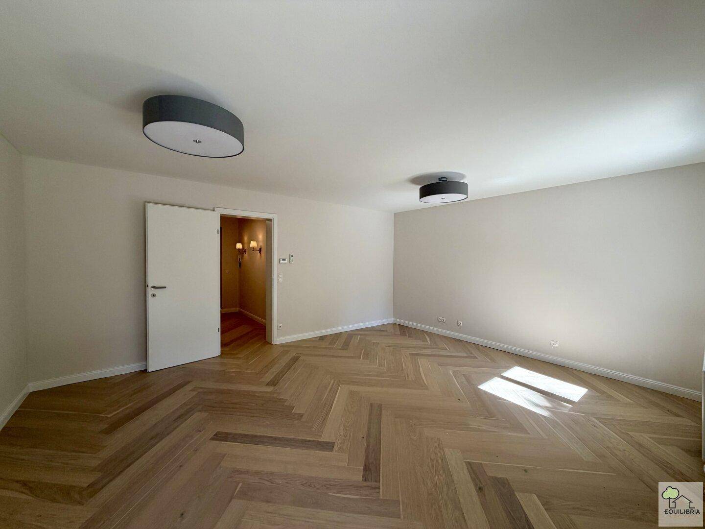 Geräumiges Wohnzimmer mit Fischgrätparkett und neutralen Wänden, bereit zur individuellen Gestaltung.