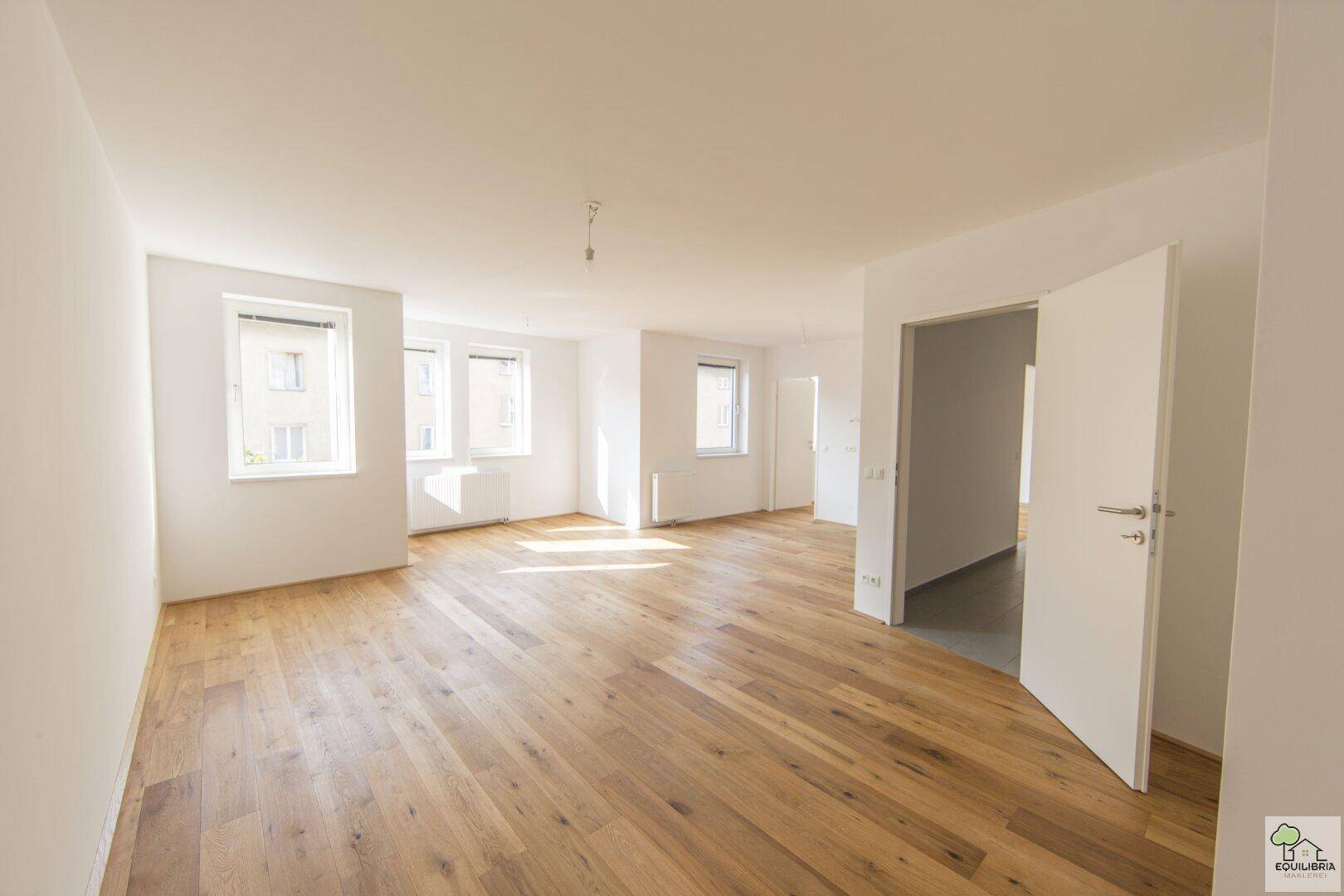 Heller, geräumiger Wohnbereich mit Eichenparkettboden und viel Tageslicht durch große Fenster.